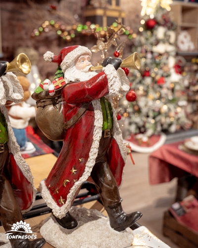Figurine de Père Noël avec trompette et sapin de Noël en fond.